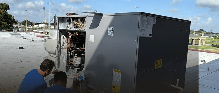Technician servicing an open commercial rooftop HVAC unit