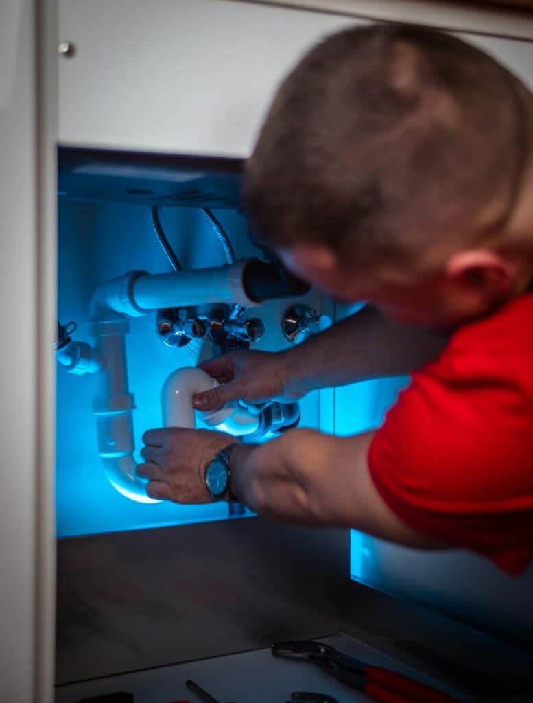 Plumber working on supply lines inside an under-sink cabinet during a general plumbing repair